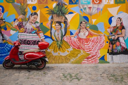 Colorful mural on a city street featuring traditional dancers with a red scooter parked in front.