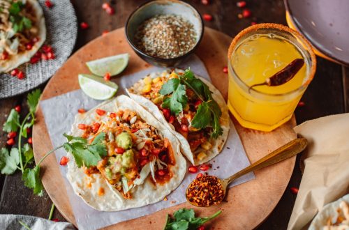 Delicious Mexican tacos served with fresh guacamole and tangy lemonade on a wooden board.