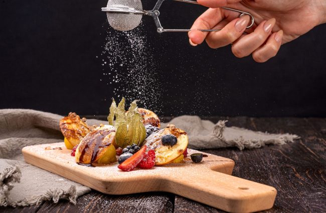 Close-up of pancakes topped with berries and dusted with sugar on a wooden board.